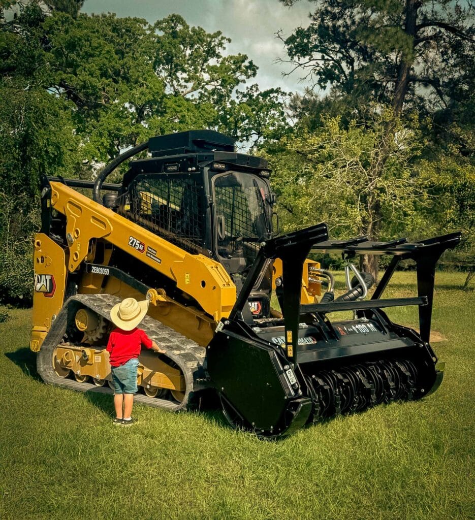 Cat 275 XE compact track loader with forestry mulching drum attachment, with a young boy in a cowboy hat looking on, Navasota, TX