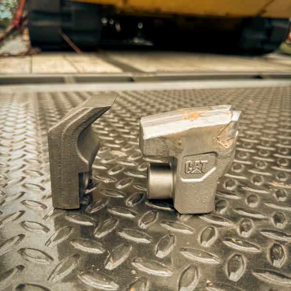 Forestry mulcher knife and carbide tooth standing on end, showing their cutting profiles.