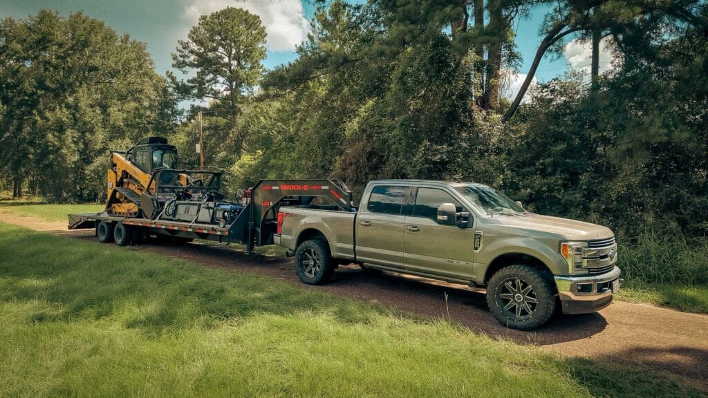 Tracked forestry mulcher loaded on a trailer behind the company truck on a cleared site