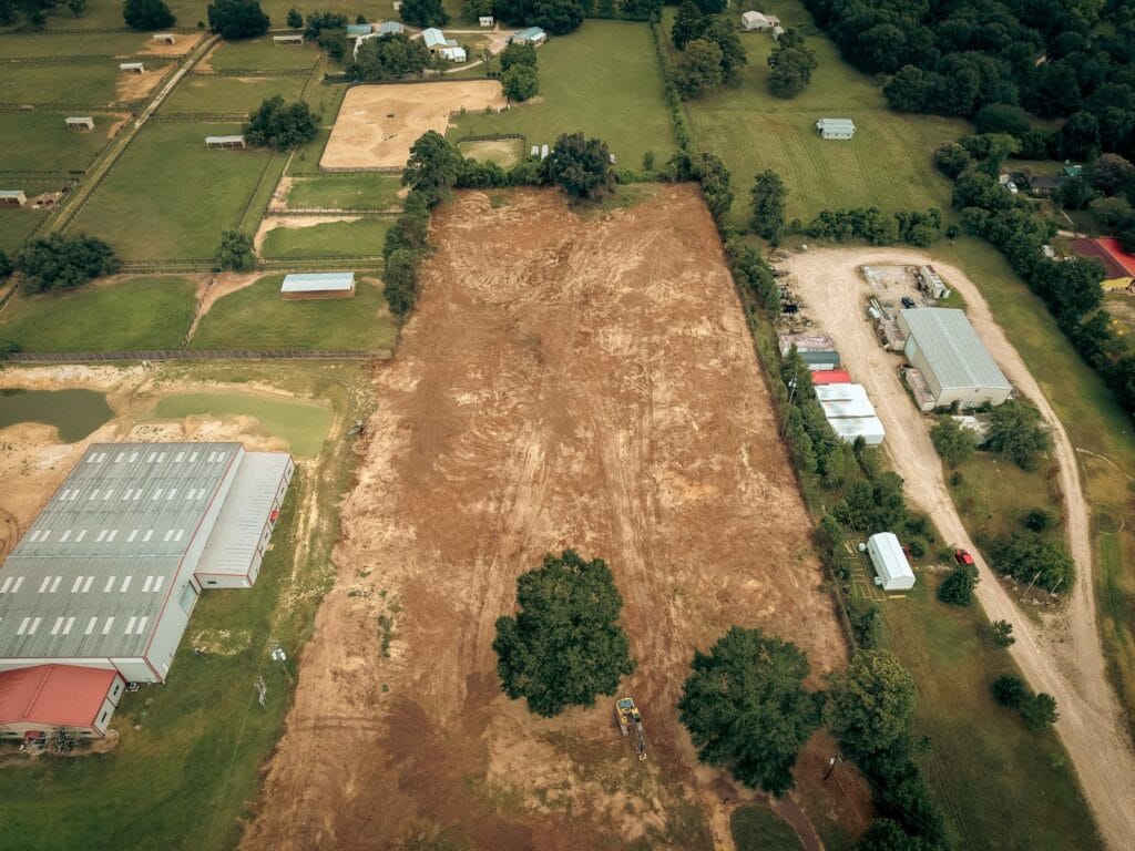 The same lot from the air after land clearing, bare graded ground the length of the property with two mature oaks left standing, near Navasota, TX