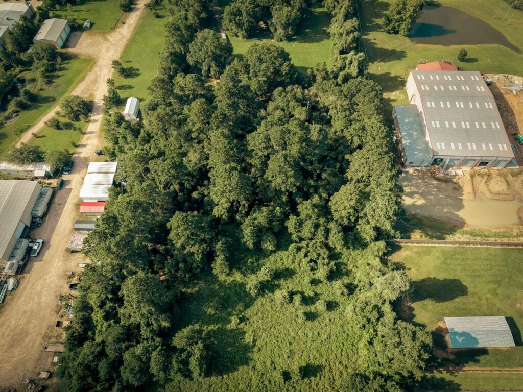 Aerial view of the opposite end of the same wooded lot before clearing, unbroken tree canopy running up to a metal building, near Navasota, TX