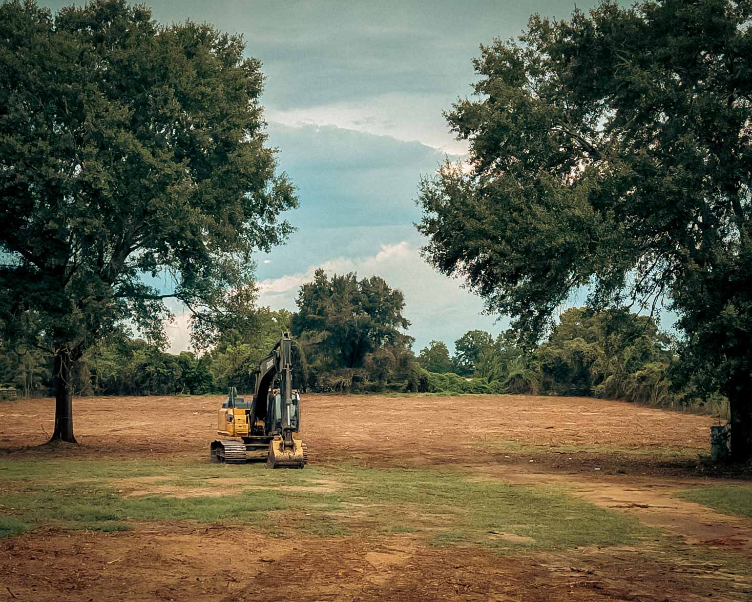 Excavator on a cleared building pad with mature oaks left standing, near Navasota, TX